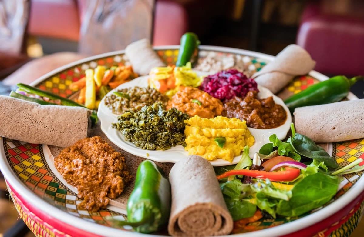 A round platter of vegan dishes on injera with rolled injera and green peppers